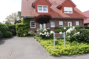 A two-story house with a red-tiled roof, a brick facade, and a paved driveway leading to the entrance. - Holiday home with 2 bedrooms (Wangerland-Hooksiel)