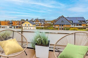 A balcony with wicker chairs and cushions, overlooking a row of modern houses. - Apartment with 1 bedroom (Wenningstedt)