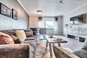 A modern living room with a sofa, coffee table, and a TV mounted on the wall. - Modern 3-room holiday apartment "Beach-Time" (Hörnum)