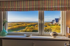 Ein Fenster mit Blick auf eine Landschaft, einem gestreiften Vorhang und zwei Vasen auf dem Fensterbrett.
