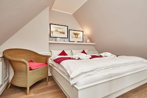 Ein Schlafzimmer mit einem Bett, einem Korbsessel und zwei gerahmten Bildern an der Wand.