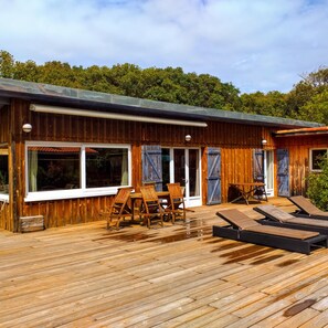 A wooden cabin with a deck, large windows, and outdoor seating. - New Listing (Lège-Cap-Ferret)