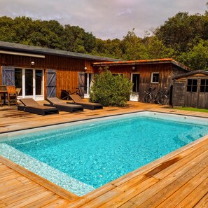 A rectangular swimming pool with a wooden deck, surrounded by a wooden building with sliding glass doors. - New Listing (Lège-Cap-Ferret)