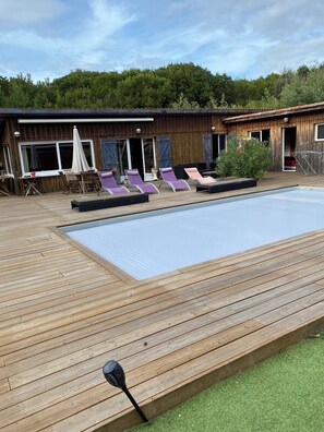A wooden deck with a pool, lounge chairs, and a building with windows and doors. - New Listing (Lège-Cap-Ferret)