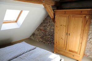 A bedroom with a sloped ceiling, a skylight, a wooden wardrobe, and a stone wall. - Holiday apartment with 1 bedroom (Meißen)