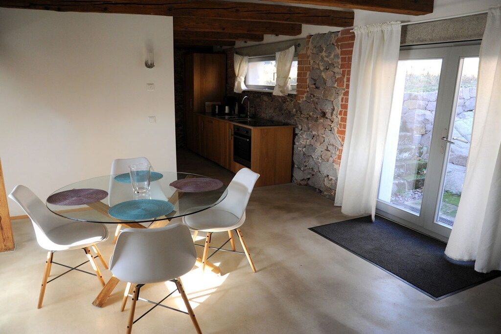 A dining area with a glass table and chairs, a kitchen with stone walls, and a view through a glass door.