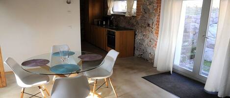 A dining area with a glass table and chairs, a kitchen with stone walls, and a view through a glass door.