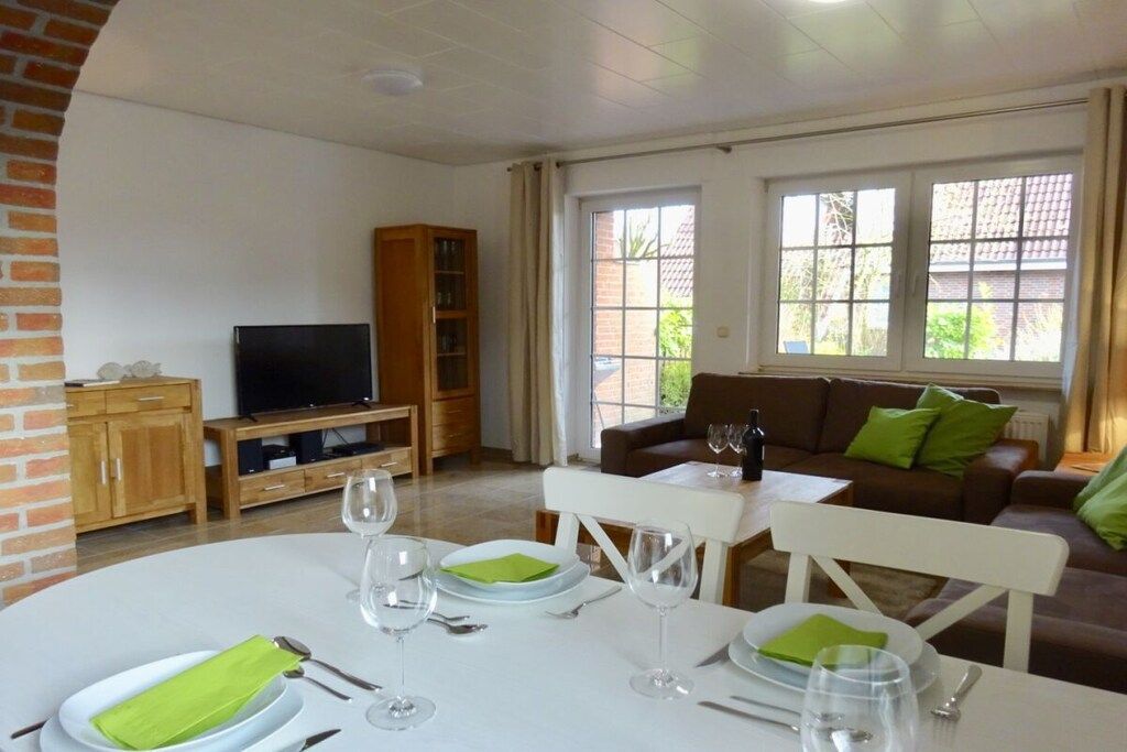 A furnished living room with a dining table set for four, a television, and a bookshelf.