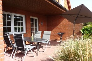 An outdoor patio with a table and chairs, a barbecue grill, and a large umbrella. - FH North Sea Feeling LD 113a (Hooksiel)