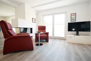 A modern living room with a sofa, armchair, and a TV on a stand. - Holiday apartment with 1 bedroom (Norden)
