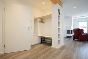 A room with a white door, a wooden floor, a red chair, and a TV stand. - Holiday apartment with 1 bedroom (Norden)