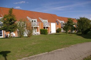 A row of residential buildings with a flat roof, a paved driveway, and a grassy area with trees. - Holiday apartment with 1 bedroom (Insel Poel, OT Kirchdorf)