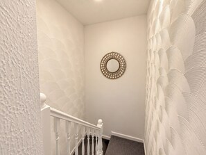 A staircase with a white railing, a wall-mounted circular mirror, and a textured wall. - Spacious 3BDR Home with Free Parking Sleeps 6 (Basildon)