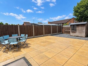 A patio with a wooden fence, a small shed, and a table with chairs. - Spacious 3BDR Home with Free Parking Sleeps 6 (Basildon)