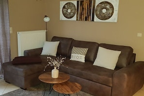 A brown leather sofa with white and patterned cushions, a small round wooden table with a vase of dried flowers, and a radiator on the wall. - Holiday apartment with 2 bedrooms (Karlshagen)
