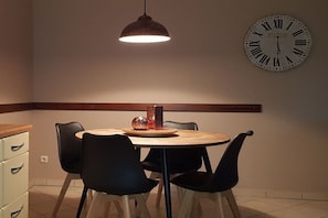 A dining area with a round table, black chairs, a pendant light, and a wall clock. - Holiday apartment with 2 bedrooms (Karlshagen)