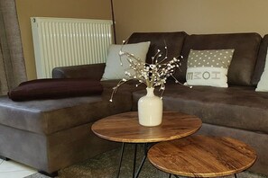 A living room with a brown sofa, two round wooden tables, and a vase with branches. - Holiday apartment with 2 bedrooms (Karlshagen)