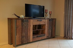 A wooden entertainment center with a flat-screen TV, two decorative candles, and a small decorative item on top. - Holiday apartment with 2 bedrooms (Karlshagen)