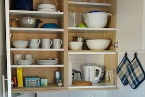 A kitchen with shelves holding various dishes, a kettle, and kitchen utensils. - Apartment with 1 bedroom (Wenningstedt\/Sylt)