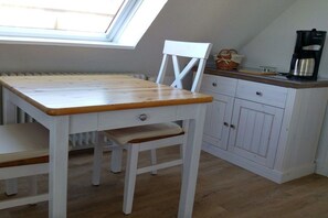 A small kitchenette with a wooden table, white cabinets, and a window. - Apartment with 1 bedroom (Wenningstedt\/Sylt)