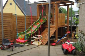 A wooden play structure with a slide and climbing area, a tricycle, and a small red vehicle. - Heinisch family with pool (Ringenhain)