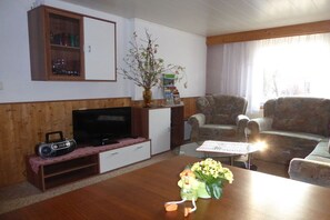 A living room with a television, a radio, a coffee table with flowers, and a bookshelf. - Heinisch family with pool (Ringenhain)