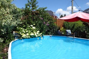 A swimming pool with a wooden deck, surrounded by lush greenery and a red umbrella. - Heinisch family with pool (Ringenhain)
