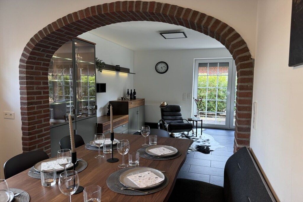 A dining area with a brick archway, a kitchen in the background, and a view of the outdoors through a glass door.