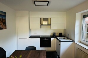 A compact kitchen with a dishwasher, a sink, and a stove. There is a dining table with chairs. - Holiday home with 3 bedrooms (Wangerland)