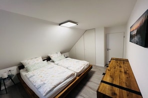 A bedroom with a bed, bedside tables, a wooden bench, and a ceiling light. - Holiday home with 3 bedrooms (Wangerland)