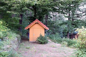 A wooden shed with a red roof, surrounded by dense greenery and trees. - Holiday home with 1 bedroom (Markersbach \/ Bad Gottleuba-Berggießhübel)