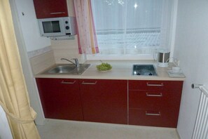 A compact kitchenette with a microwave, sink, and a window with sheer curtains. - Holiday apartment with 2 bedrooms (Bodensdorf)