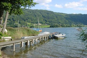 A lake with boats docked at a wooden pier, surrounded by greenery and hills. - Holiday apartment with 2 bedrooms (Bodensdorf)