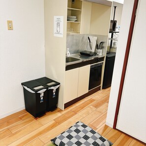Une petite cuisine équipée comprenant un four à micro-ondes, un évier et des placards de rangement. On y trouve également deux poubelles et un petit tapis sur le sol.