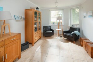 A living room with a wooden cabinet, two black leather sofas, a small round table, and a lamp. - The house at the southern end of the spa park (Norderney)