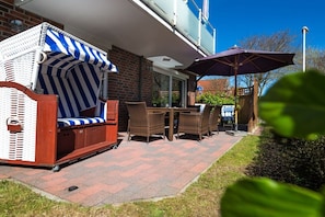 An outdoor seating area with wicker furniture and a striped awning. - The house at the southern end of the spa park (Norderney)