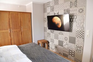 A bedroom with a bed, a wooden wardrobe, a television mounted on a patterned wall, and a small wooden stool. - Holiday apartment with 1 bedroom (Lübbenau)