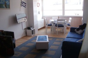 Ein Wohnzimmer mit einem blauen Sofa, einem kleinen weißen Tisch und einem Fernseher an der Wand.