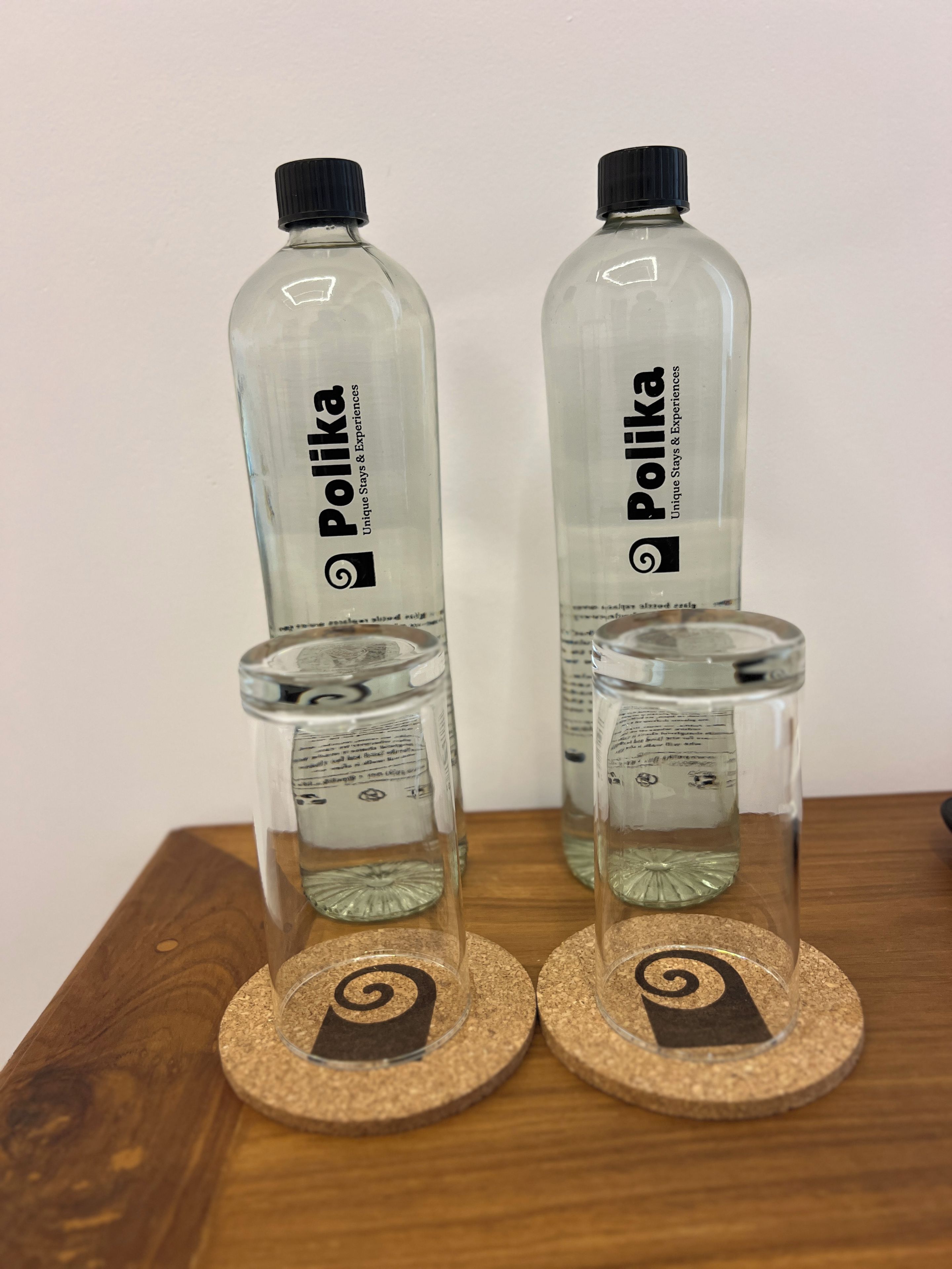 Two Polka water bottles and two clear glasses on coasters with a spiral design.