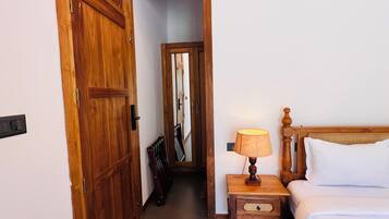 A hotel room with a wooden door, a bedside table with a lamp, and a bed with white bedding.