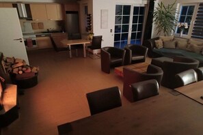 A modern living room with a sofa, chairs, a dining table, and a kitchen in the background. - Holiday home with 5 bedrooms (Ueckermünde)