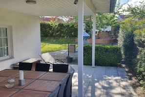 A covered patio with a table and chairs, a white fence, and a hedge. - Holiday home with 5 bedrooms (Ueckermünde)