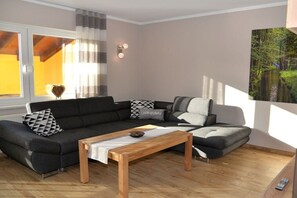 A modern living room with a sectional sofa, a wooden coffee table, and a painting of a forest scene. - Holiday apartment with 2 bedrooms (Lübbenau)