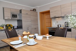 A modern kitchen with wooden cabinets, a microwave, and a dining table set for breakfast. - Holiday apartment with 2 bedrooms (Lübbenau)