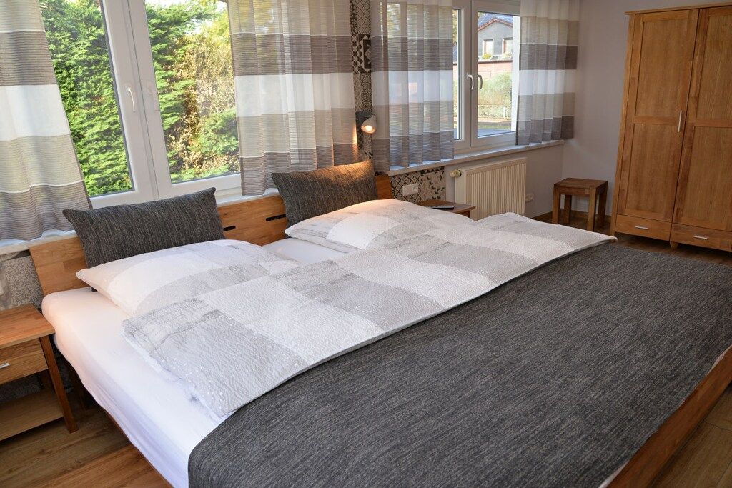 Een slaapkamer met een groot bed, twee nachtkastjes, een houten kledingkast en een raam met gordijnen.