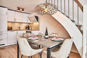 A modern kitchen with white cabinets, a dining table set for four, and a unique spiral staircase. - Holiday apartment with 2 bedrooms (Westerland)