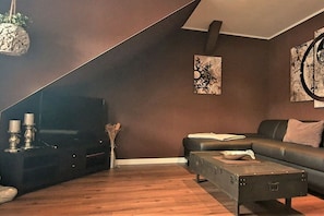 Una sala de estar moderna con una pared marrón oscuro, un sofá negro, una mesa de centro de madera y un televisor sobre un mueble negro.