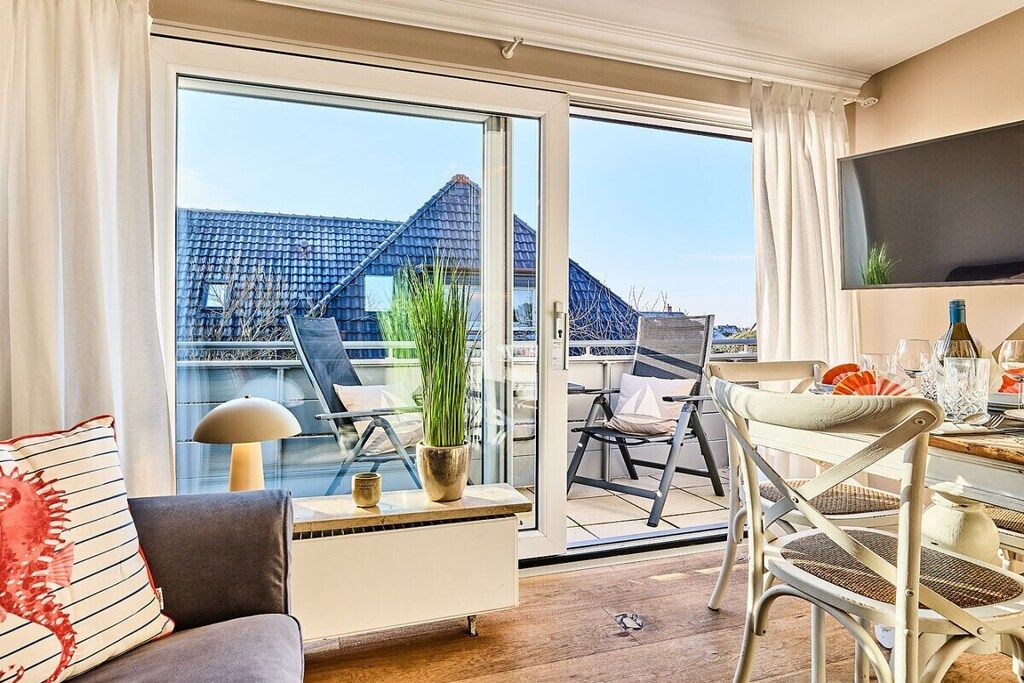 A modern living room with a sofa, a coffee table, a TV, and a balcony with a view of buildings.