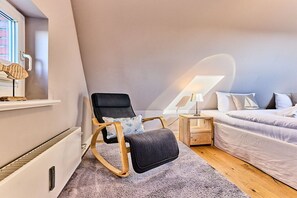 A modern bedroom with a bed, a chair, a nightstand, and a window. - Holiday apartment with 2 bedrooms (Wenningstedt)