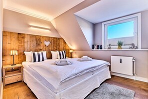 A bedroom with a large bed, wooden headboard, bedside lamps, a radiator, and a window with a view. - Holiday apartment with 2 bedrooms (Wenningstedt)